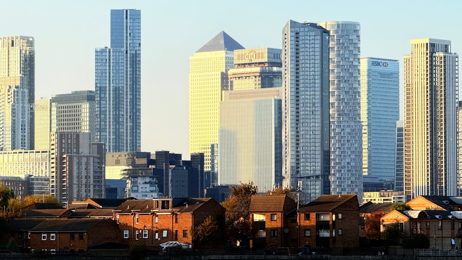 A panoramic view of a city skyline during daylight, featuring numerous modern high-rise office buildings and residential skyscrapers constructed with glass facades and steel frameworks. In the foregro